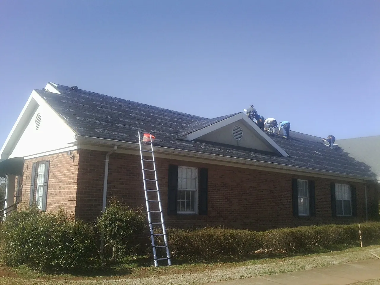 Crew tearing shingles off a brick ranch roof with a ladder set — Metal Roof Repair work by our crew in Three Rivers