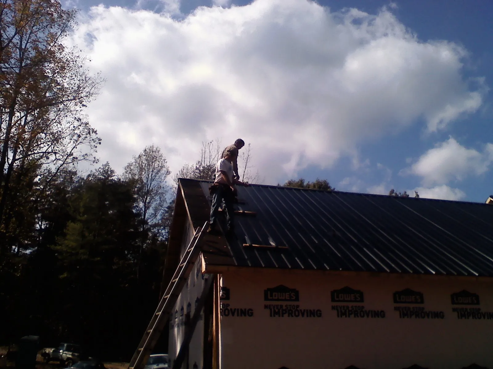 Roofer fastening dark metal panels high against a cloudy sky, from a Roof Inspection job in Three Rivers
